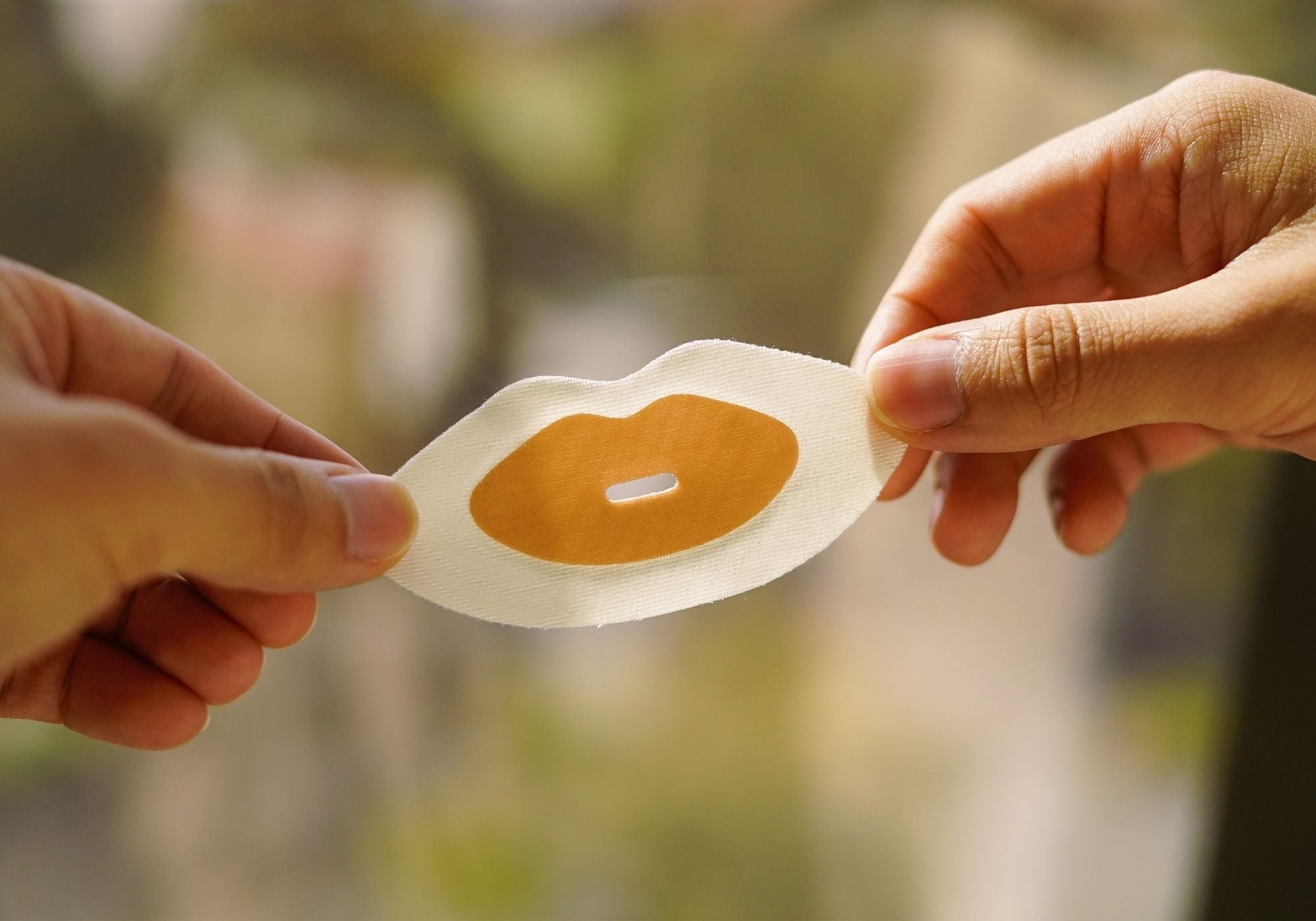 Hands holding the adhesive side of a Sayang Sleep Strip, showing the soft centre cushion, airflow slit and skin-friendly adhesive.