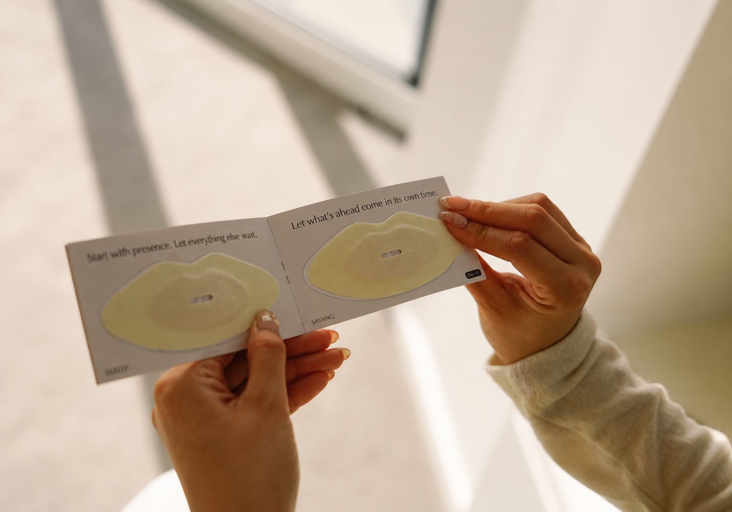Hands holding the Your Sayang Journey booklet with used Sayang Sleep Strips placed beside uplifting morning quotes.