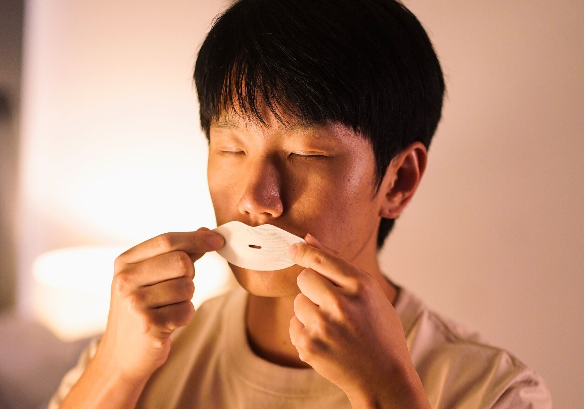 Man preparing to apply Sayang Sleep Strips during his nighttime ritual, showing mouth tape for sleeping as part of a calming bedtime routine.
