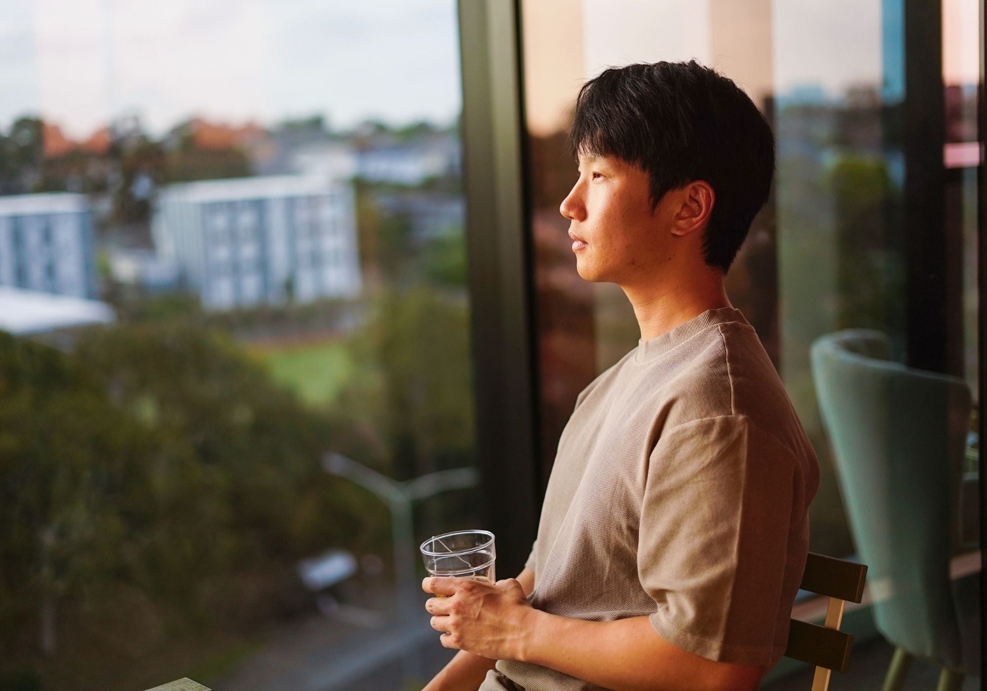 Man holding a glass by a window during a calm daytime moment, representing Week 2 of the Sayang Sleep Strips journey.