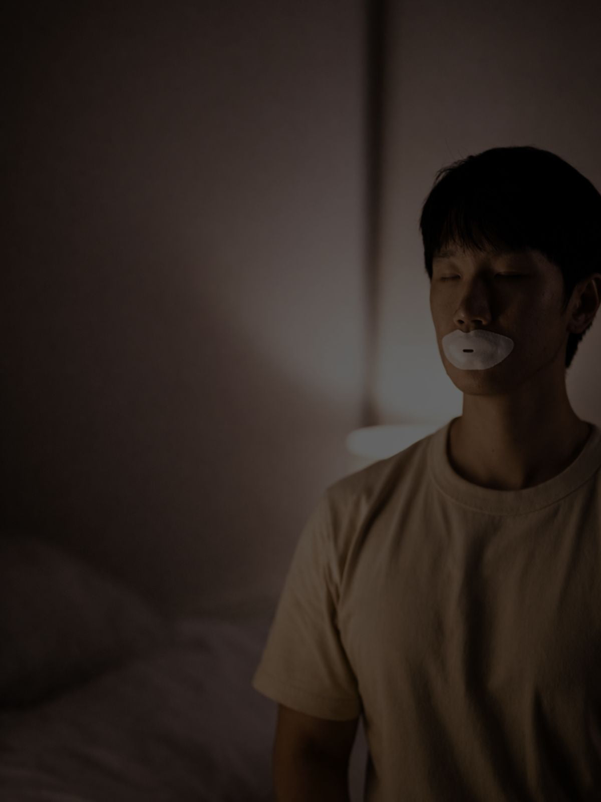 Man wearing a Sayang Sleep Strip with closed eyes in a softly lit bedroom during a calm evening nasal breathing ritual.